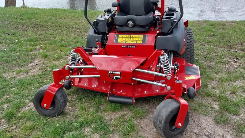 A red zero-turn riding mower parked on grass near a river